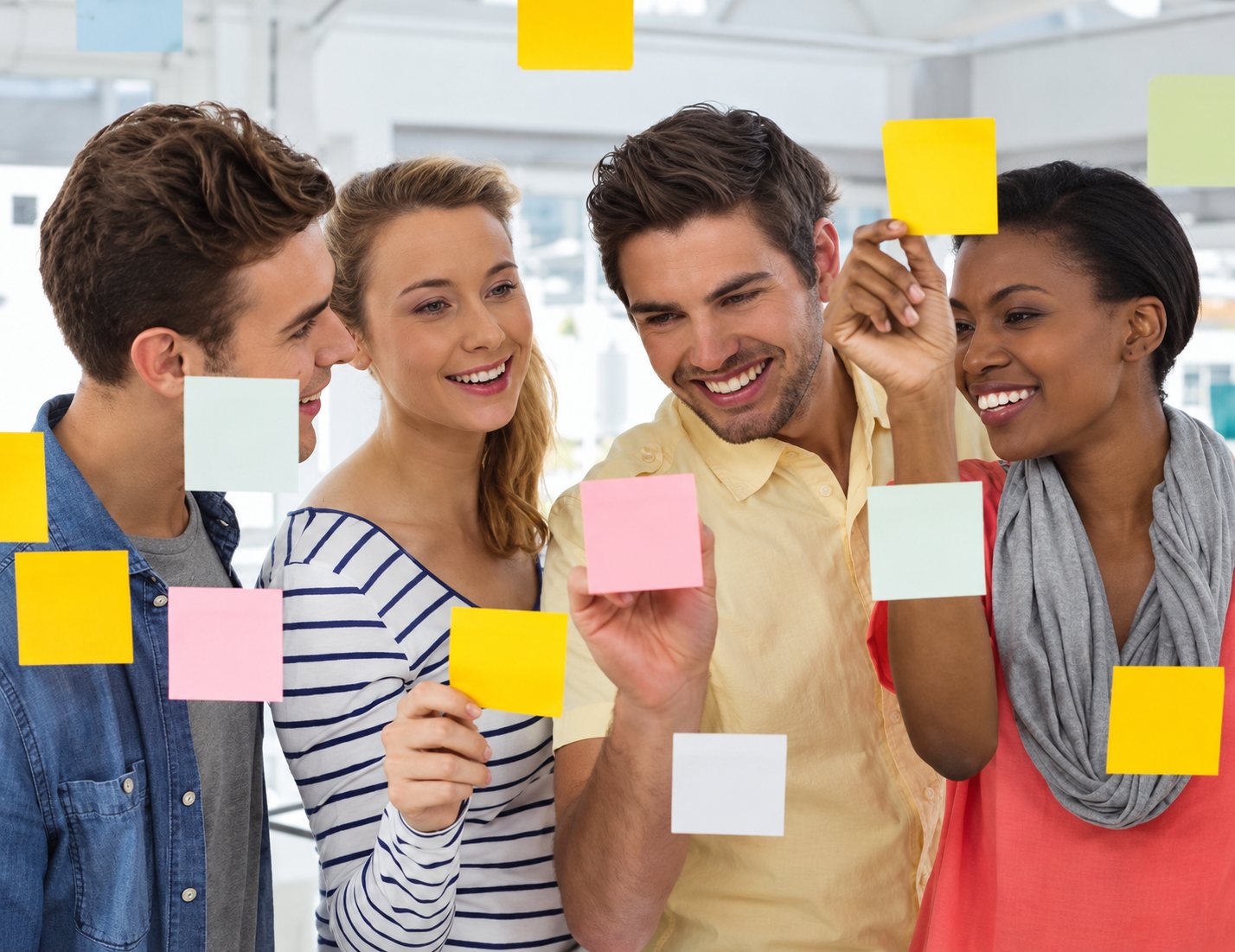 Quatre collègues souriants collent des notes adhésives sur une paroi vitrée