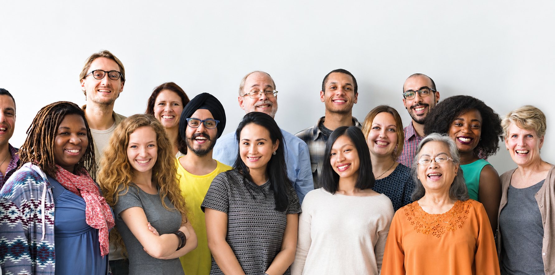 Un groupe d'hommes et de femmes de tous âges, souriants et serrés les uns contre les autres, pose devant un mur blanc.